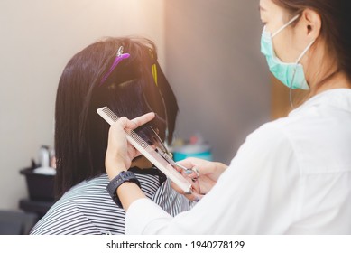 Young Asian Woman Barber Wear Green Surgical Mask, Cut Black Hair Customer. Beautiful Hairstylist Trimming Scissors In Hair Cut Salon Shop. Female Hairdresser With Face Mask Protect Working In Barber 