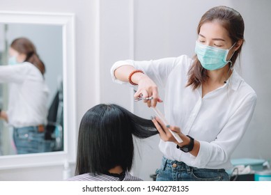 Young Asian Woman Barber Wear Green Surgical Mask, Cut Black Hair Customer. Beautiful Hairstylist Trimming Scissors In Hair Cut Salon Shop. Female Hairdresser With Face Mask Protect Working In Barber 