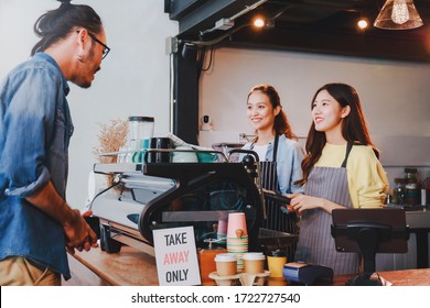 Young Asian woman barista wear apron making coffee cup served to customer at bar counter in coffee shop with smile face and takeaway orders only sign.Social distancing in situation of covid-19.