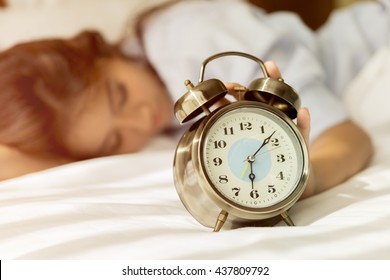 Young Asian woman in bed trying to wake up with alarm clock.