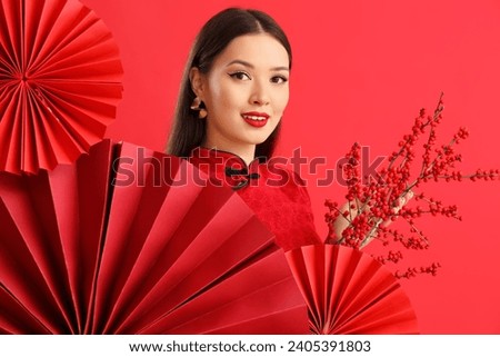 Young Asian woman with berry branches and fans on red background. Chinese New Year celebration