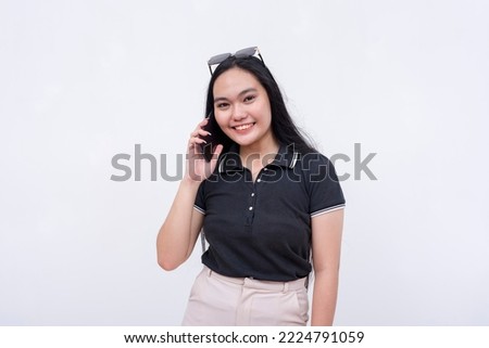 A young asian woman in a black polo shirt holding a cellphone. Calling or talking to someone on the phone. Isolated on a white backdrop.