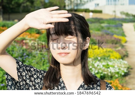 Junge Frau bedeckt ihr Gesicht vor der Sonne auf einem grünen Feld.