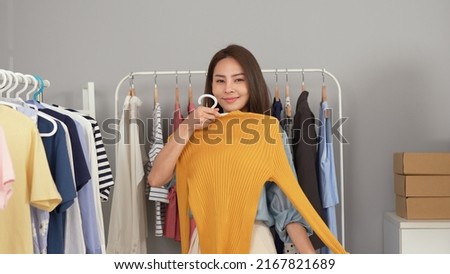 Young asian woman blogger choose clothes in the clothes rail. Start small businesses SME owners female entrepreneurs use a laptop at home,pack and delivery situation. Delivery concept.
