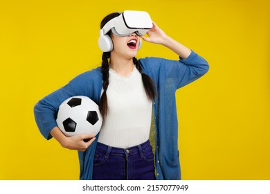 Young asian woman in blue and white shirt pigtails hairstyle wearing virtual reality headset holding a ball looking and cheering world cup soccer football game online digital. - Powered by Shutterstock