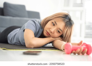 Young asian woman bored with exercise in home. Lazy asian woman exercising bored face holding dumbbells giving up fitness concept. - Powered by Shutterstock