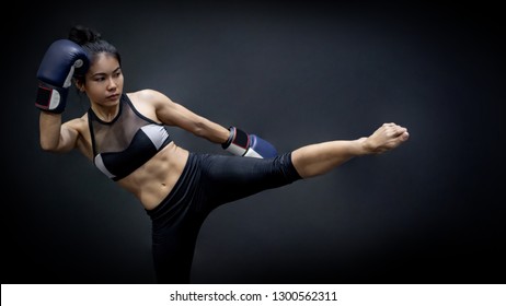 Young Asian Woman Boxer With Blue Boxing Gloves Kicking In The Exercise Gym, Martial Arts On Black Background. Female Boxing Class Concept