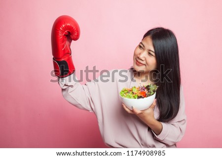 Young Asian woman with boxing glove and salad on pink background