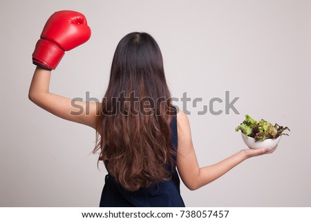 Young Asian woman with boxing glove and salad on gray background