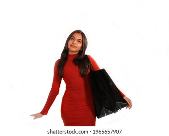 Young asian woman with brown hair in a tight red dress holds two black shopping bags and smiles.