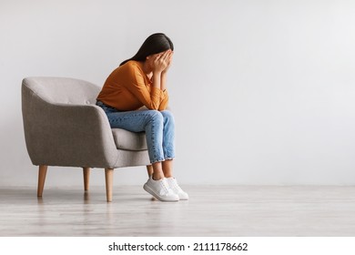 Young Asian woman burying her face in hands and crying, feeling depressed, sitting in armchair against white studio wall, copy space. Millennial lady having mental problems or mood disorder - Shutterstock ID 2111178662