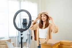 Young Asian Woman Business Owner At Fashion Store Using Cellphone Live Streaming For Sale Fashion Hat And Clothing. Influencers Record Video Review Item For Sell On Social Media. Online Shopping