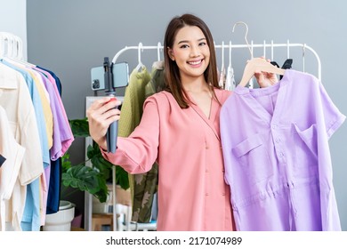 Young Asian Woman Business Owner At Fashion Store Holding Smartphone Live Streaming For Sale Fashion Clothing. Blogger Review Clothes For Presenting On Social Media. Online Shopping Concept.