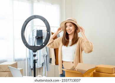 Young asian woman business owner at fashion store using cellphone live streaming for sale fashion hat and clothing. Influencers record video review item for sell on social media. Online shopping - Shutterstock ID 2337713037