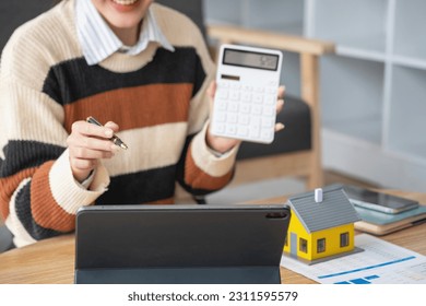 Young Asian woman calculating the cost of selling a house and analyzing the return on real estate investments. Real estate accounting concepts and tax system. - Shutterstock ID 2311595579