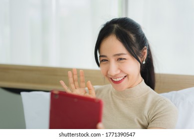 Young Asian Woman In Casual Outfit With Smile Happy Face Holding Tablet To Use Communication And Facetime Video Call With Other People At Home In Bedroom