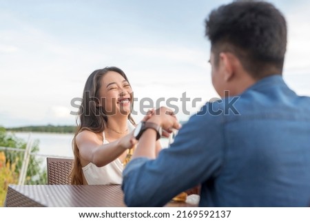 A young asian woman chuckles and holds her dates hand after being teased. Signs of attraction during a first date. Showing a sense of humor.
