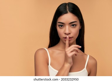 Young Asian woman with clean healthy glowing skin in white top isolated on beige background. Facial skin care concept, spa, cosmetology, plastic surgery.