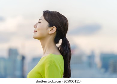 Young asian woman closing eyes in front of the city.