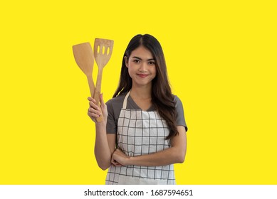 Young Asian Woman Cook Holding A Wooden Spatula Isolated On Yellow Studio Background