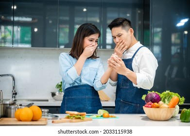 Young Asian Woman Crying In Pain Due To A Knife Cut In Finger While Chopping Vegetables In Kitchen With Husband Looking At Wound Shockingly At Home