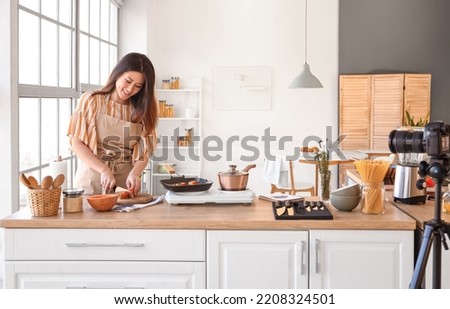 Young Asian woman cutting pumpkin while recording video class in kitchen