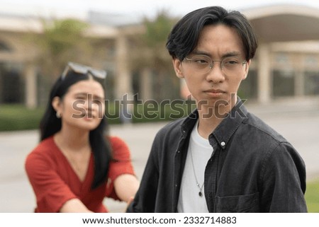 A young asian woman desperately holds on to her upset boyfriend, imploring him not to leave her. A breakup scenario initiated by the man.