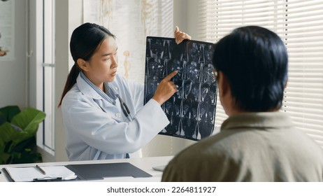 Young Asian woman doctor showing lung x-ray test results and describe to a senior patient in hospital. For cancer awareness month - Powered by Shutterstock