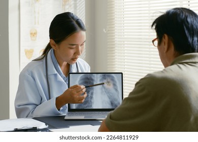 Young Asian woman doctor showing lung x-ray test results and describe to a senior patient in hospital. For cancer awareness month - Powered by Shutterstock