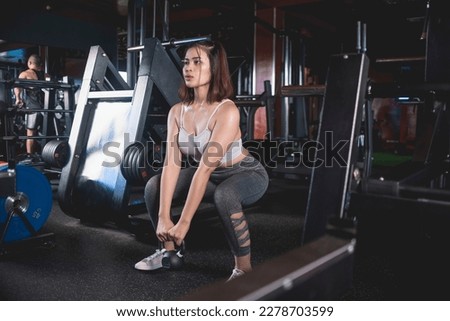 A young asian woman does a set of plie squats with a kettlebell. Training at a modern gym.