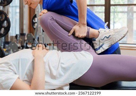 young asian woman doing leg stretch with physical therapist in personal gym