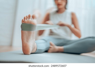 Young Asian woman doing pilates workout using elastic strap pulling with arms for shoulder training on yoga mat indoors. Resistance band exercise at home - Powered by Shutterstock