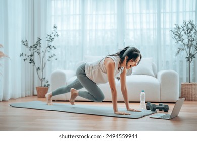 Young Asian woman doing sport exercises indoor. Beautiful girl workout at home. Athletic outfit is doing mountain climber exercises - Powered by Shutterstock