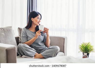 Young Asian Woman Drinking Coffee On A Sofa Bed At Home