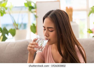 Young Asian woman drinking water and taking pill while sitting on sofa at home. Asian woman stressed and sick 