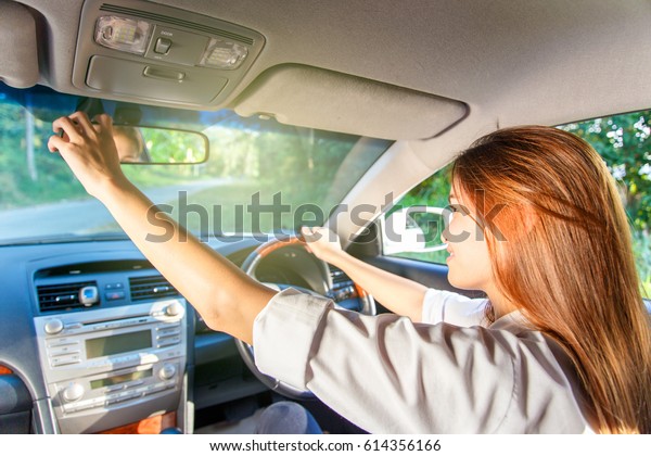 Young asian woman driver adjusting her rearview\
mirror in the car.