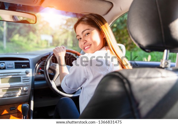 Young asian woman driver driving a car on\
the road in countryside.