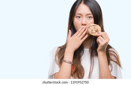 Young Asian Woman Eating Chocolate Chip Cookie Over Isolated Background Cover Mouth With Hand Shocked With Shame For Mistake, Expression Of Fear, Scared In Silence, Secret Concept