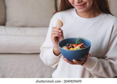 A Young Asian Woman Eating Healthy Blueberry Smoothie Bowl With Mixed Fruits Topping On Sofa At Home