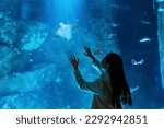 Young Asian woman enjoy and fun learning and looking sea life at Aquarium on holiday vacation. Attractive girl looking shoal of fish and aquatic animals in large glass tank during travel in Oceanarium