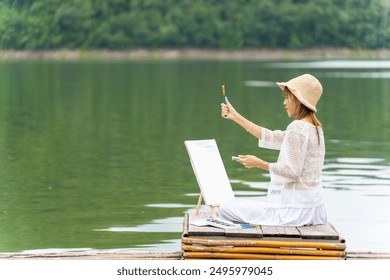  Young Asian woman enjoy and fun outdoor lifestyle travel nature forest mountain on summer holiday vacation. Happy girl relaxing with hobbies drawing and painting watercolor on lake house balcony. - Powered by Shutterstock