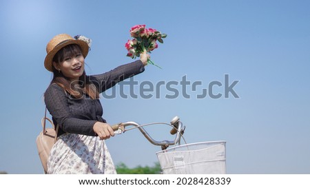 young asian woman enjoying cycling holding flowers in park