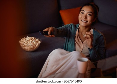 Young Asian woman enjoying in the evening at home while eating popcorn and watching a movie. 