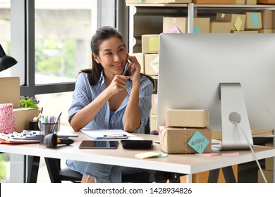 Young Asian Woman Entrepreneur/ Business Owner Using A Smartphone And Working With Computer At Home