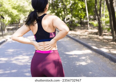 Young Asian woman exercising in the park Pain in the back and using a hand to hold on my back That hurts while experiencing severe pain: exercise injury concepts - Powered by Shutterstock