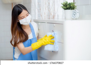 Young Asian Woman In Face Mask And Gloves Cleaning Home In Room, Housekeeper Is Wipe With Fabric, Housemaid And Service, Worker Polish Dust In House, Housework And Domestic, Lifestyle Concept.