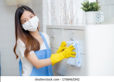 Young Asian Woman In Face Mask And Gloves Cleaning Home In Room, Housekeeper Is Wipe With Fabric, Housemaid And Service, Worker Polish Dust In House, Housework And Domestic, Lifestyle Concept.