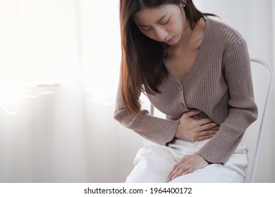 Young Asian woman feel sick and suffering from strong abdominal pain stomachache or period comes or lactose intolerant while sitting on the chair at home