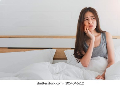 Young Asian woman feel toothache and discomfort on bed in white bedroom morning.Concept of women's health care.