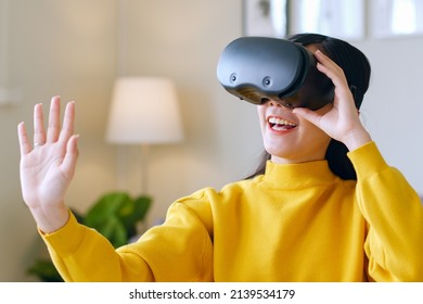 Young Asian woman feeling excited while using 360 VR headset for virtual reality, Metaverse at home 